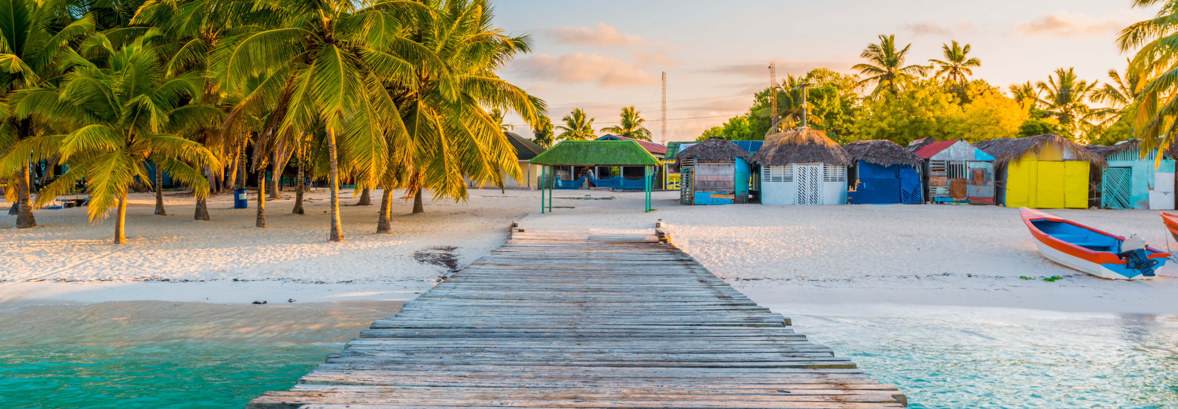 A vibrant row of beach huts and a wooden pier set against the backdrop of a tropical island paradise in the Dominican Republic