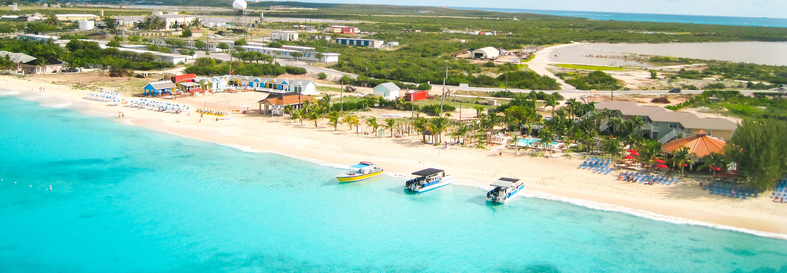Stunning shoreline in Turks and Caicos with turquoise water, boats ashore on the sand, and colorful dwellings