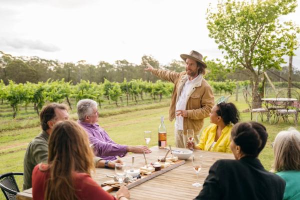 Group of people seated outdoors as a winemaker explains vineyard views