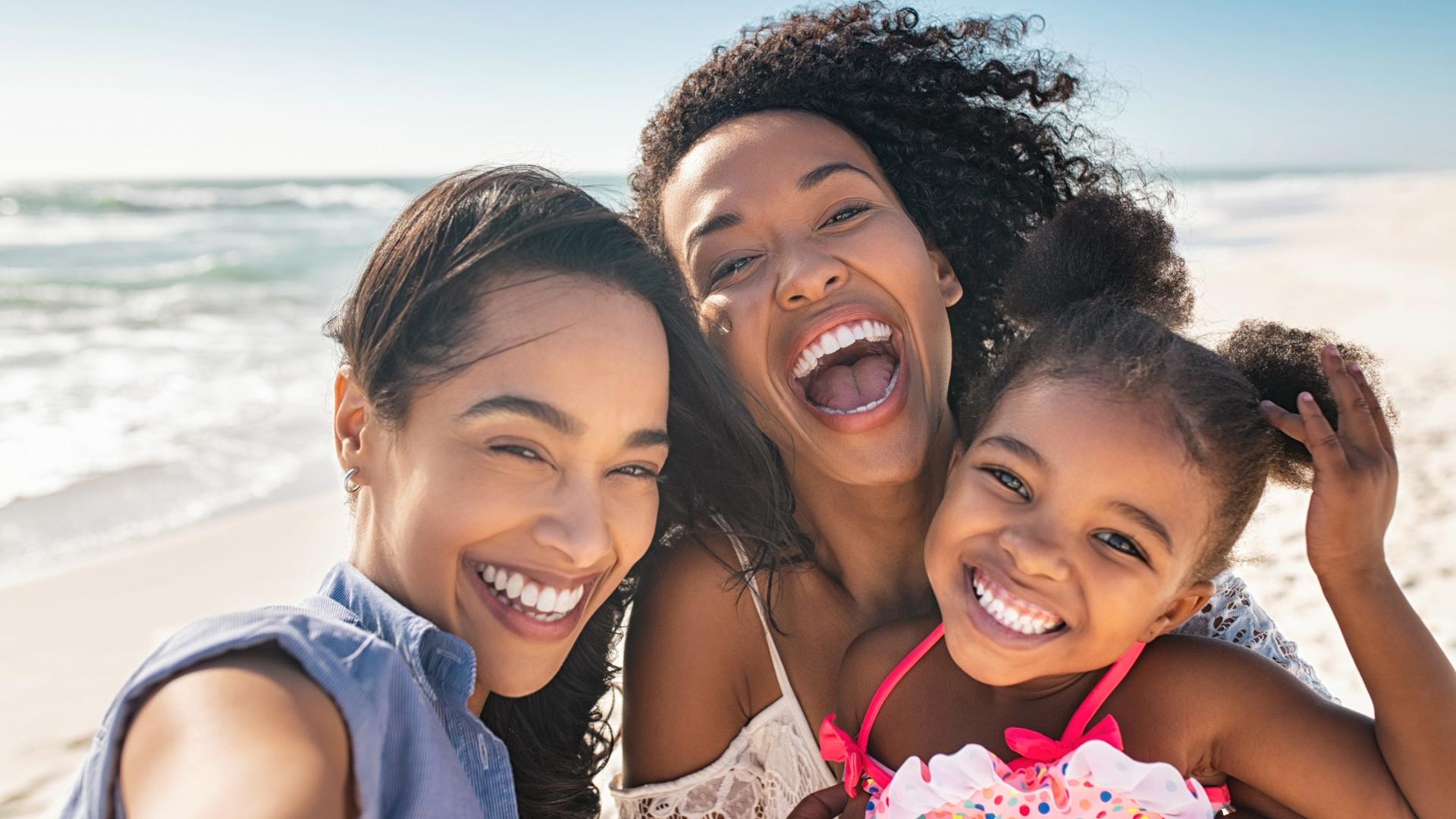 Family smiling together while taking a photo on a sunny beach.