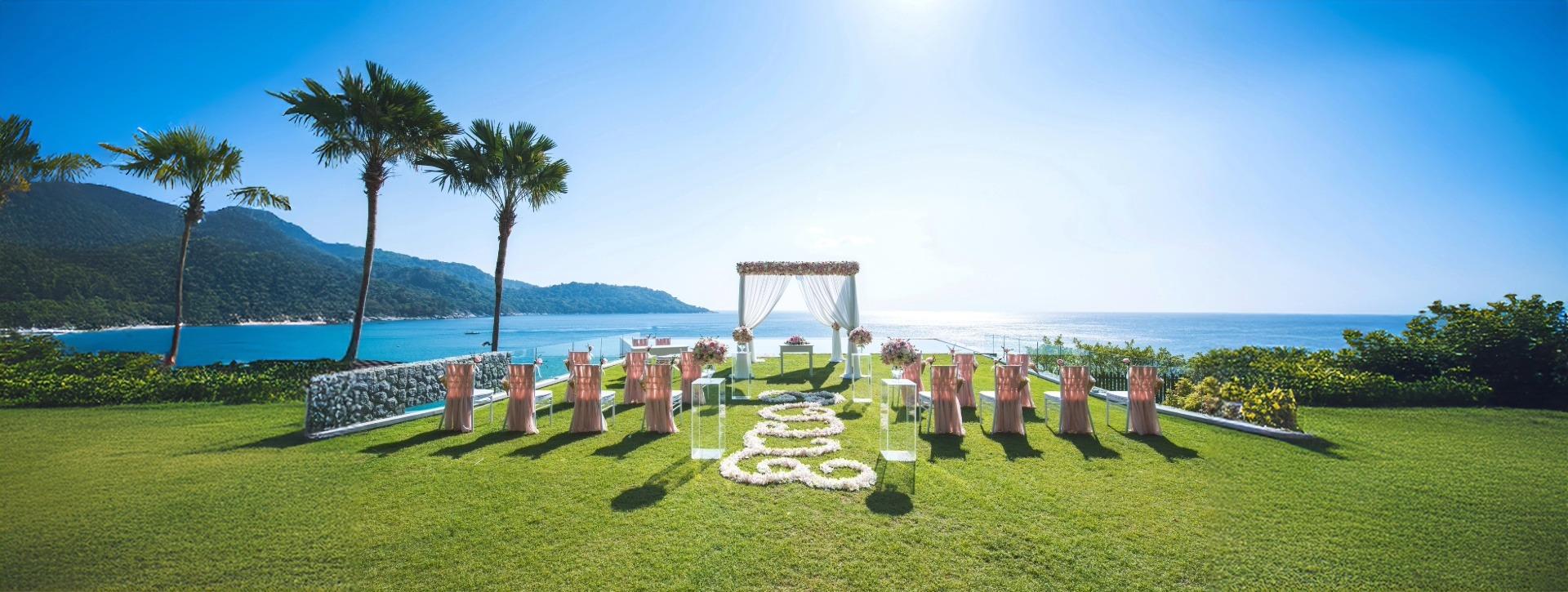 Outdoor wedding altar with pink chairs on lawn facing ocean view
