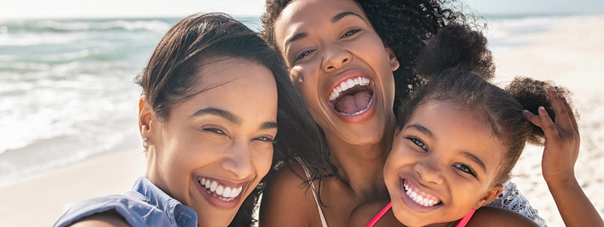 Family smiling together while taking a photo on a sunny beach.