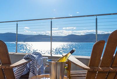 Two chairs and a table with a bottle of champagne and glasses on a cruise desk looking towards the open sea