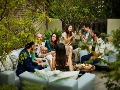 People sitting outside on couches sharing drinks and conversation with food tray nearby