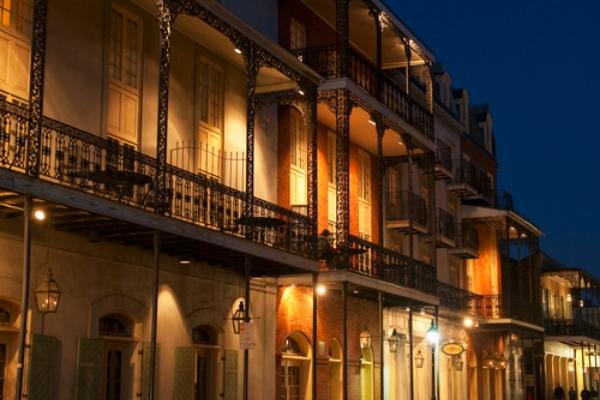 Row of historic buildings with balconies lit by warm lights at night in New Orleans.