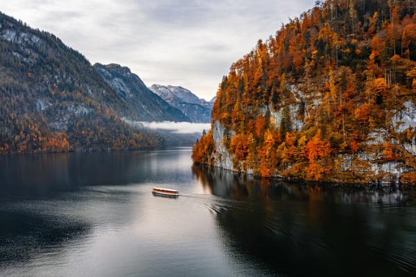 Small boat crossing a mountain lake surrounded by autumn trees and cliffs.