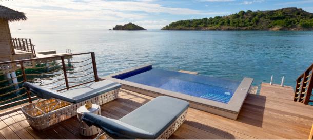 Overwater bungalow deck featuring a private plunge pool, two lounge chairs, and a stunning ocean view, promoting a Royalton Black Friday resort offer.