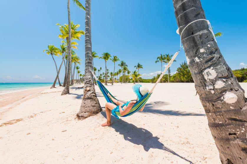 Person lying in a hammock between palm trees on a bright, sandy beach