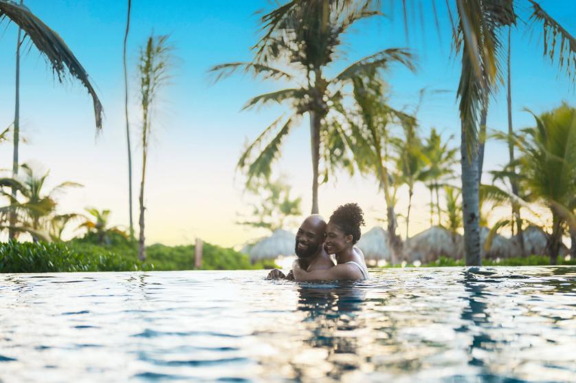 Smiling couple in a pool surrounded by palm trees under blue sky