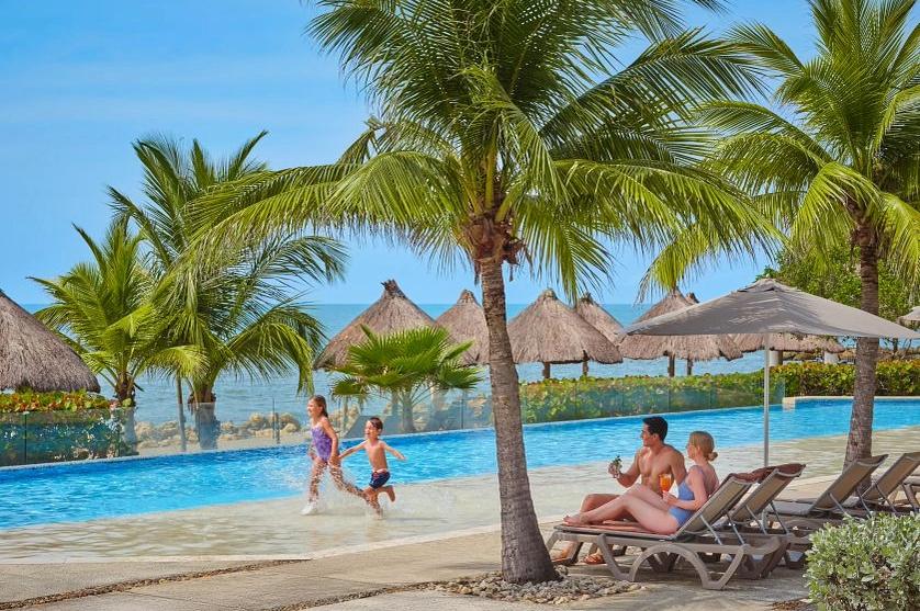 Family enjoying pool at Dreams Resorts & Spas beachfront all inclusive resort with palm trees