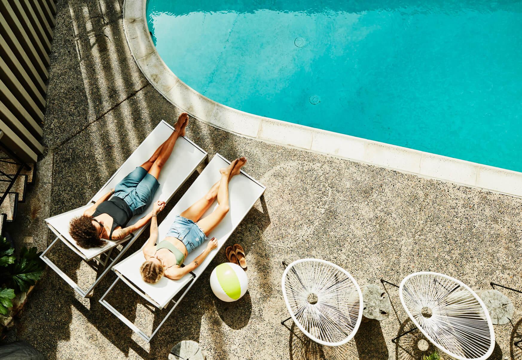 Two women hold hands while lounging poolside