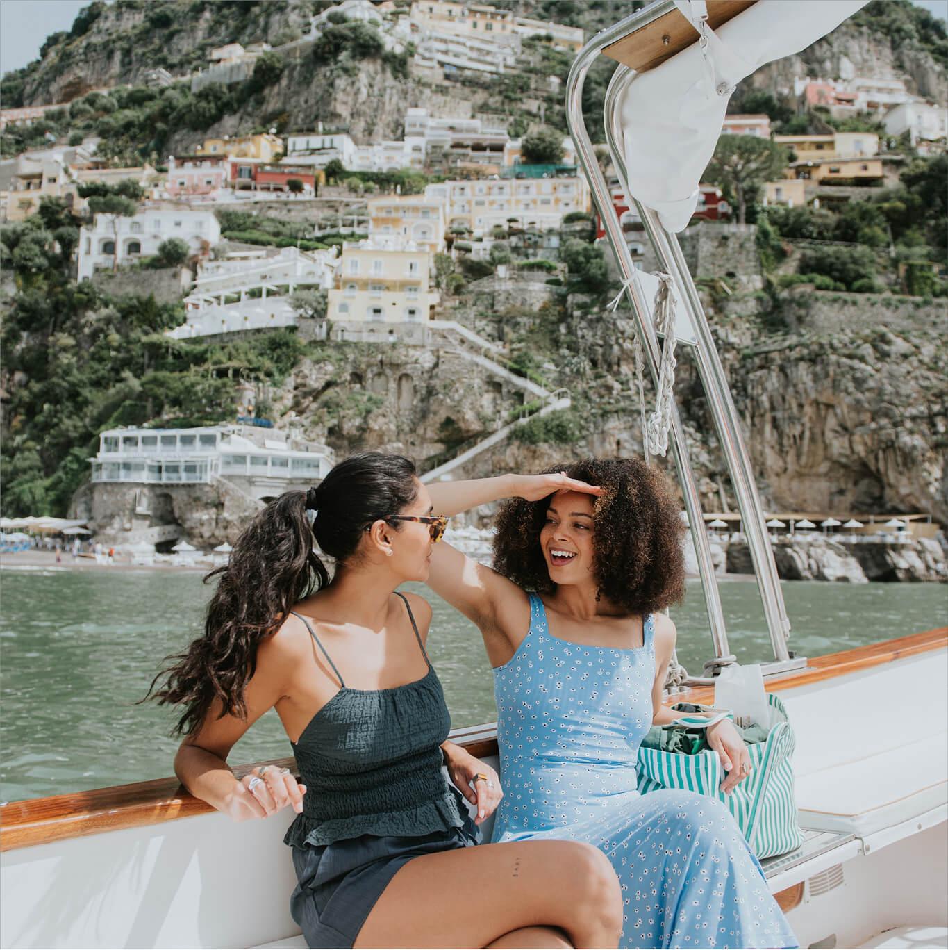 Two friends chat on a boat with the Amalfi Coast behind them