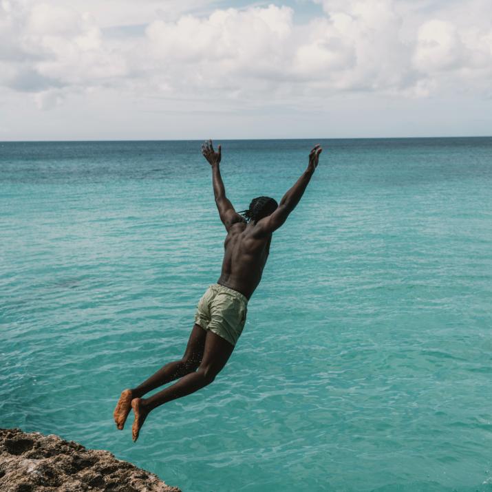Person leaping from rocks into bright blue ocean under sunny sky in Aruba.
