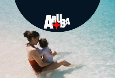 Mother and child sitting in shallow turquoise water on Aruba beach.