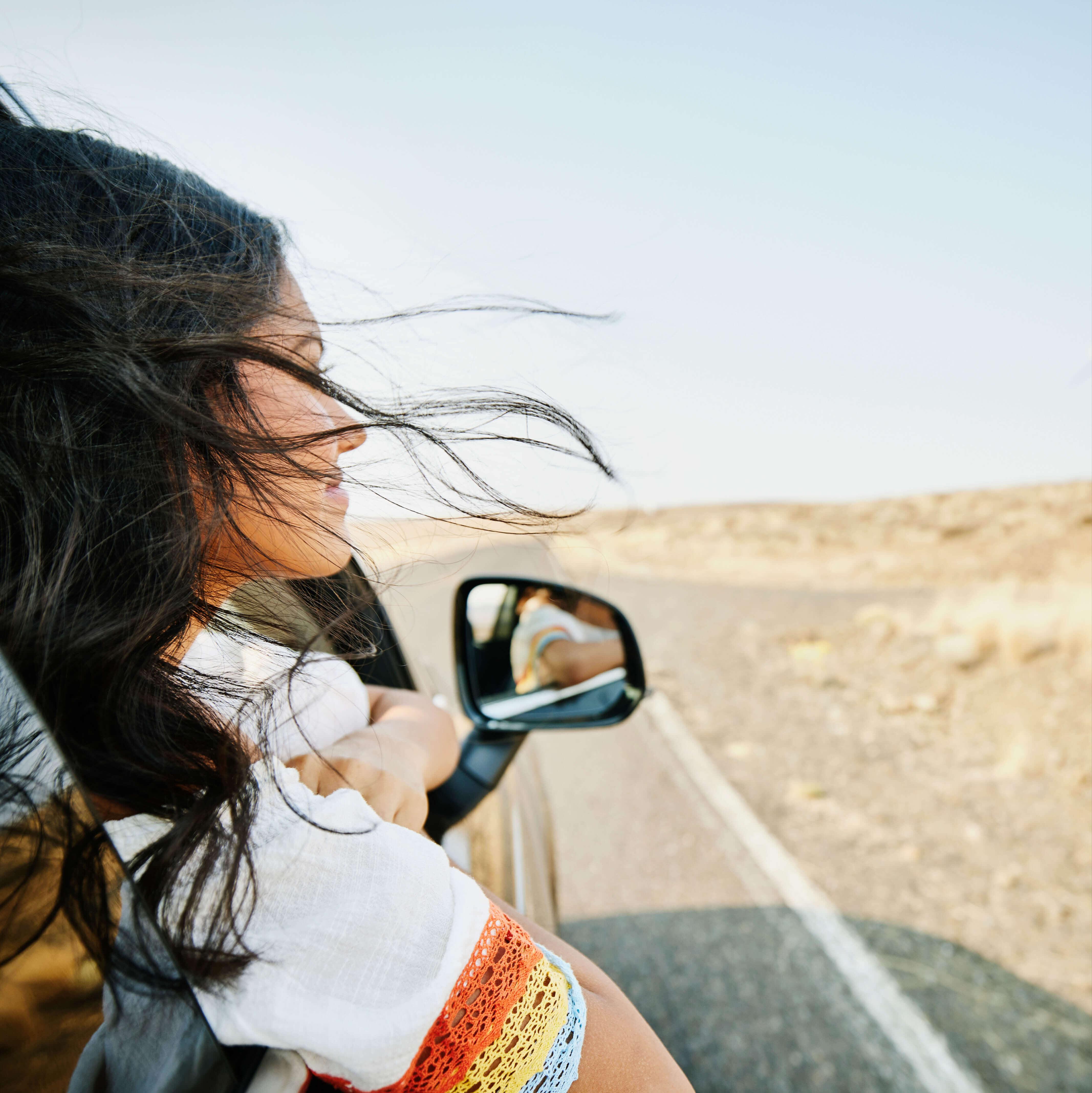 A woman looks out the window of her car along a California highway