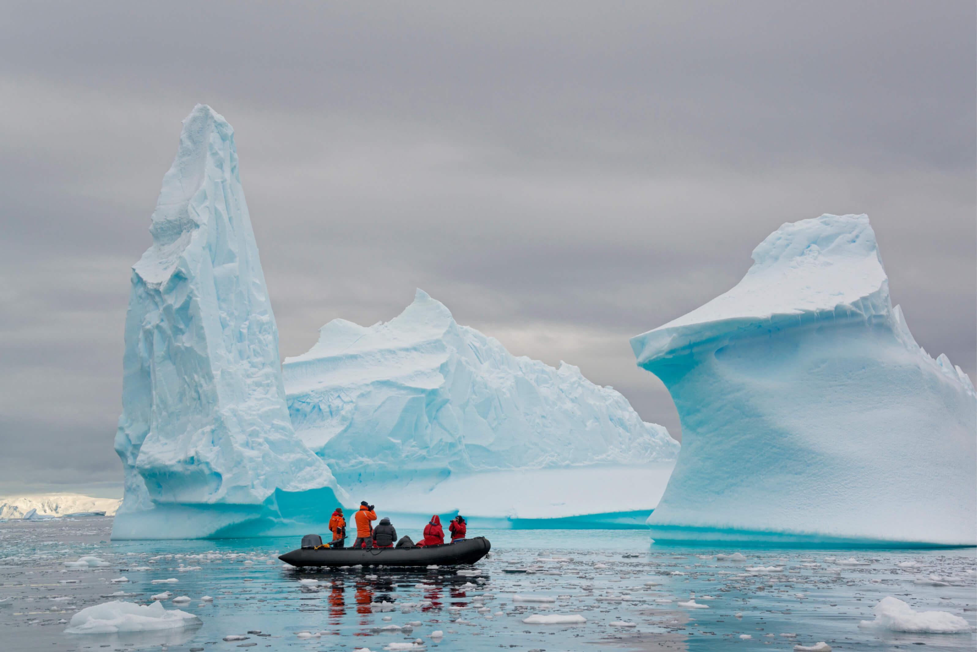 Small boat of travelers observing icebergs in Antarctica