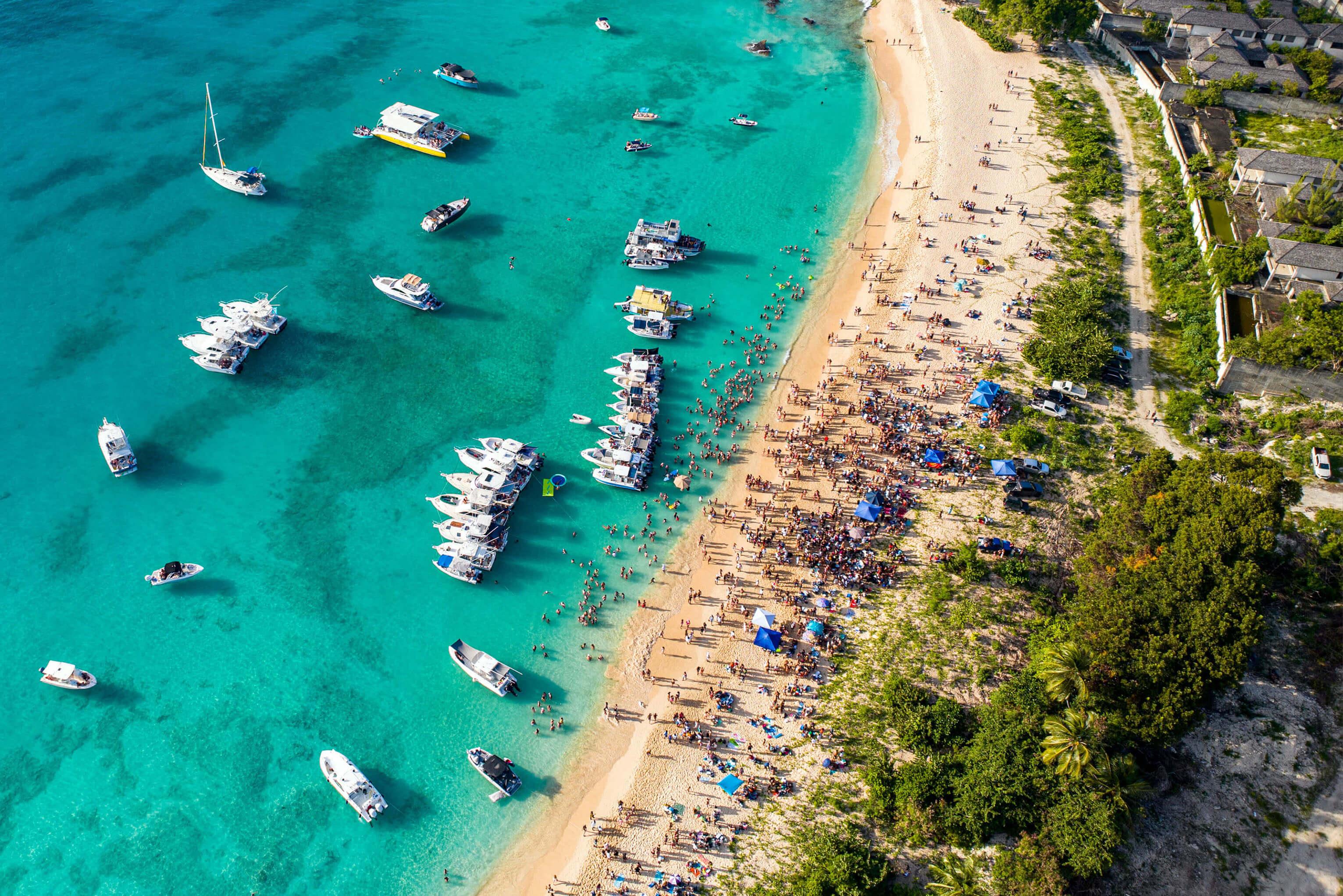 A vibrant beach with several boats anchored and people relaxing and playing along the shoreline in Barbados