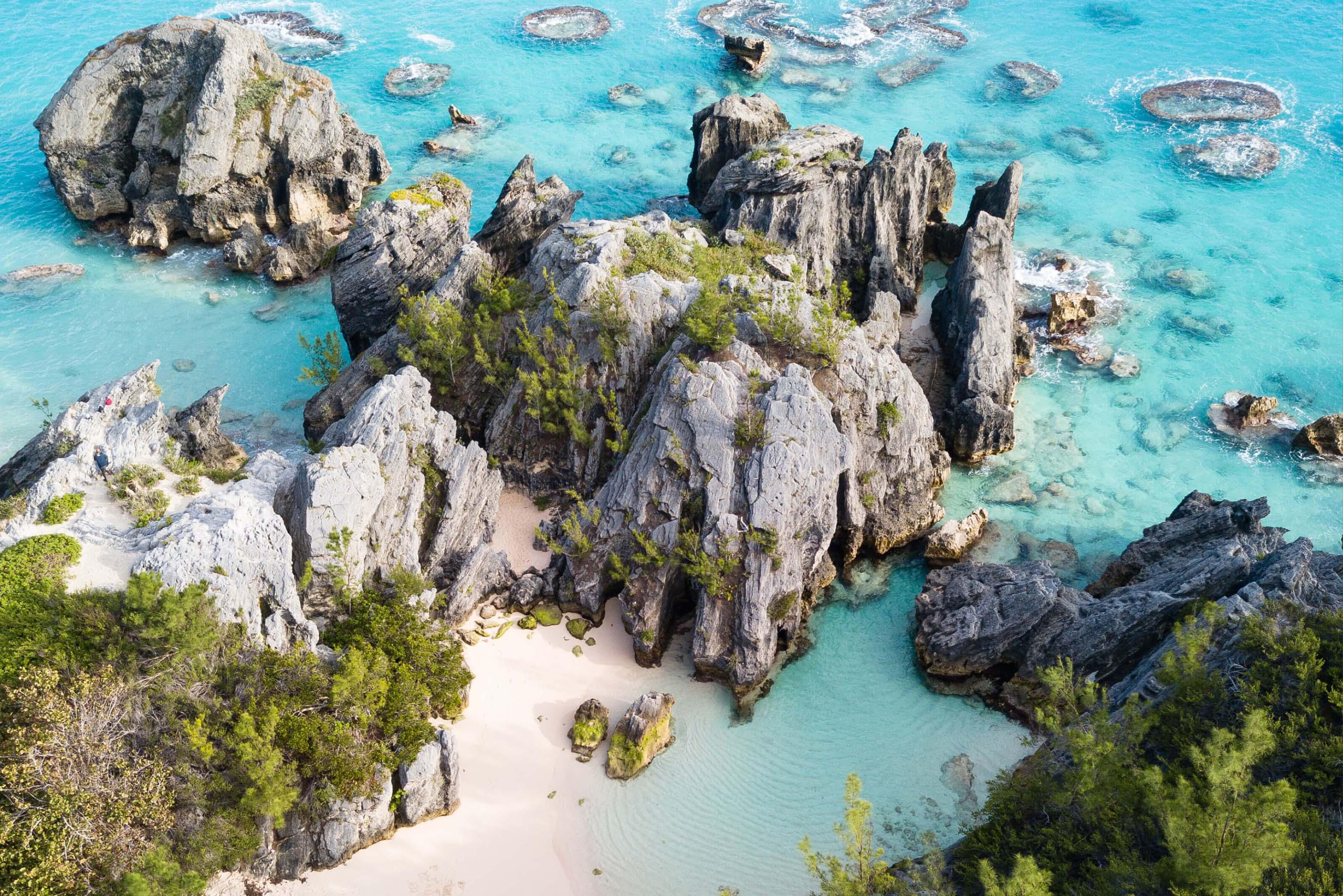 Aerial view of a beach in Bermuda featuring rocky formations and clear turquoise water lapping at the shore
