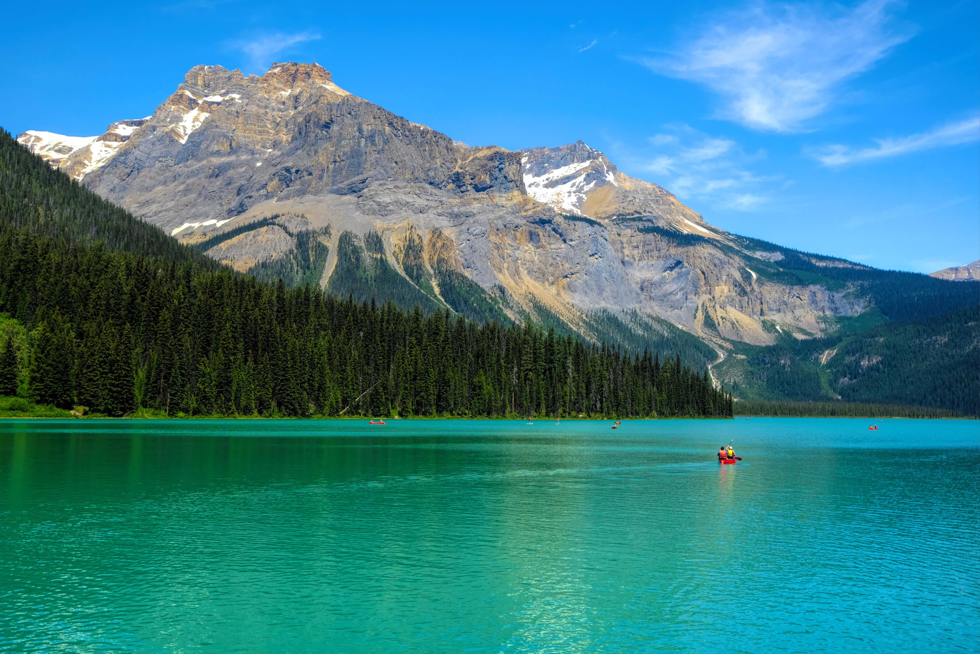 A tranquil lake in Canada with a majestic mountain in the background, surrounded by lush greenery