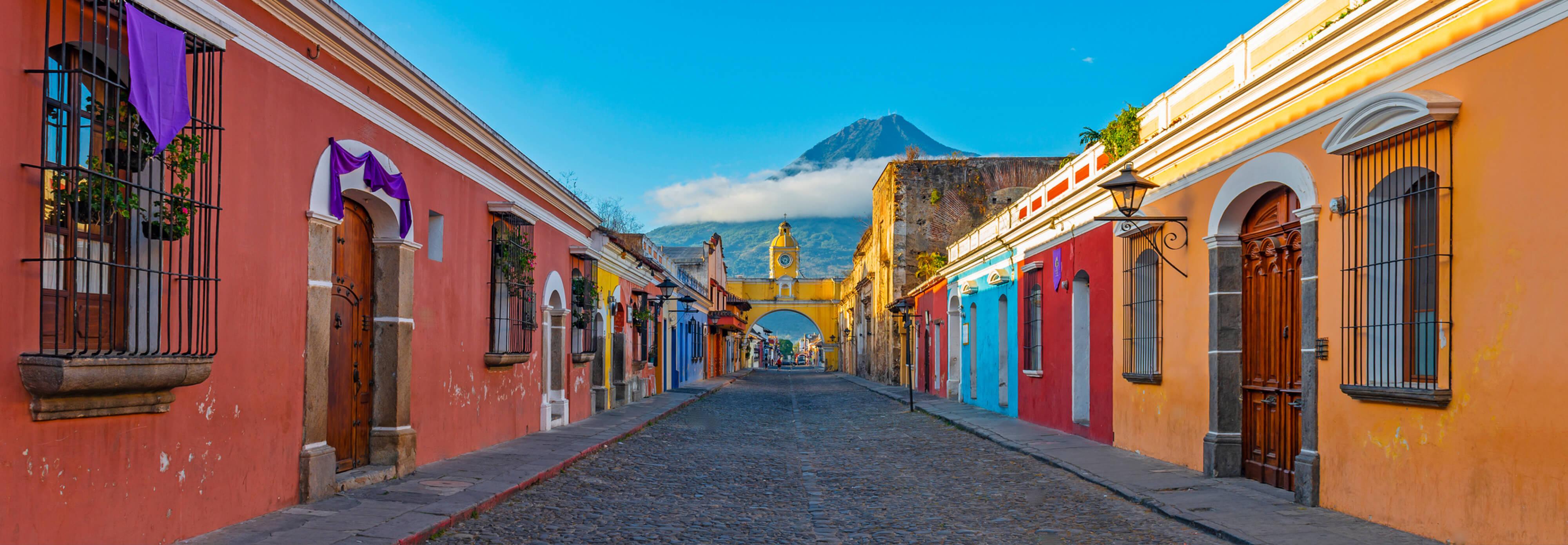 A vibrant narrow street in Central America featuring colorful buildings, set against a backdrop of a towering mountain