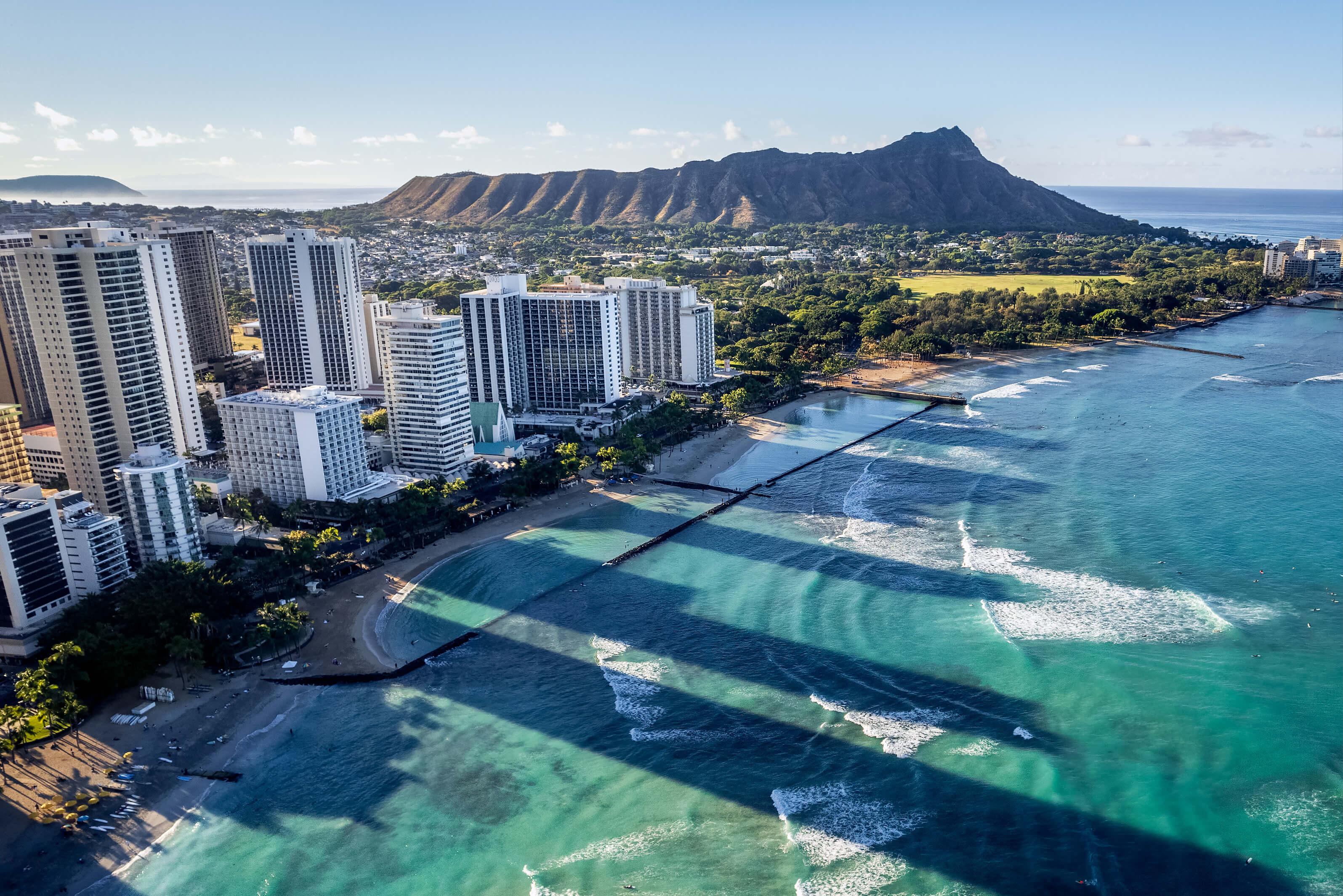 Beautiful beach in Hawaii, featuring golden sand, clear blue water, palm trees, and resorts under a bright sky
