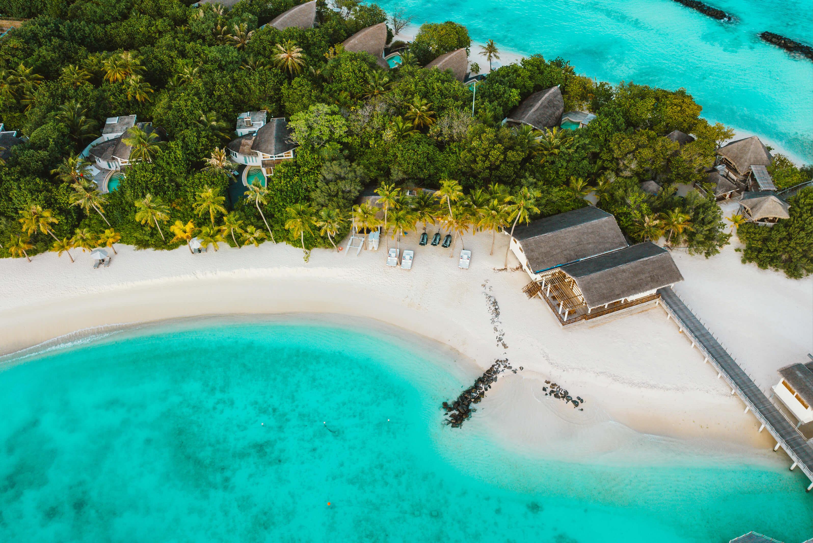 Tropical island in Indian Ocean featuring huts surrounded by lush green trees and clear blue waters