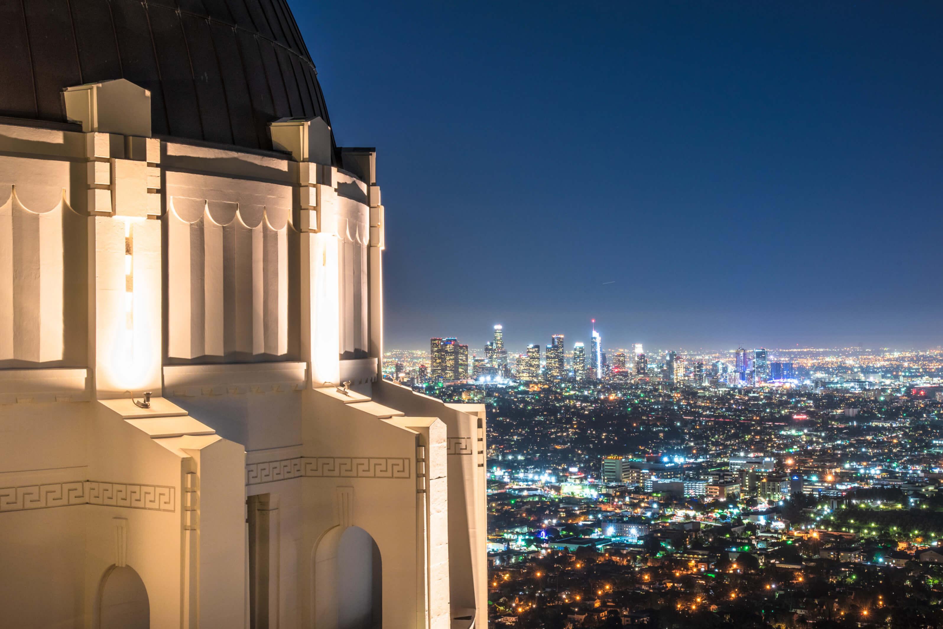Griffith Observatory illuminated at night, showcasing its iconic architecture against a starry sky with Los Angeles skyline in the background