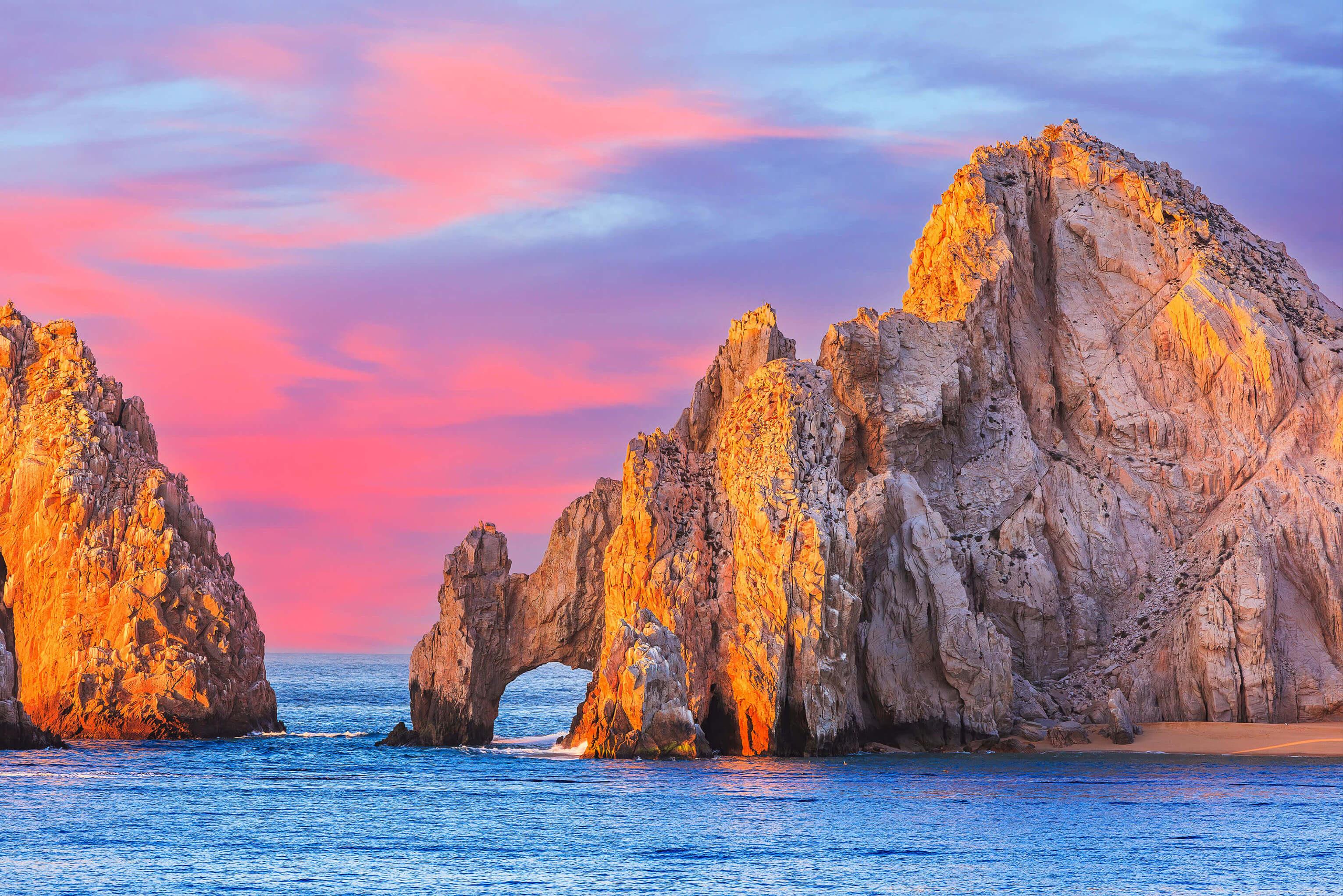 Stunning rock formations at Cabo San Lucas, Mexico, showcasing unique shapes against a pink sky and ocean backdrop