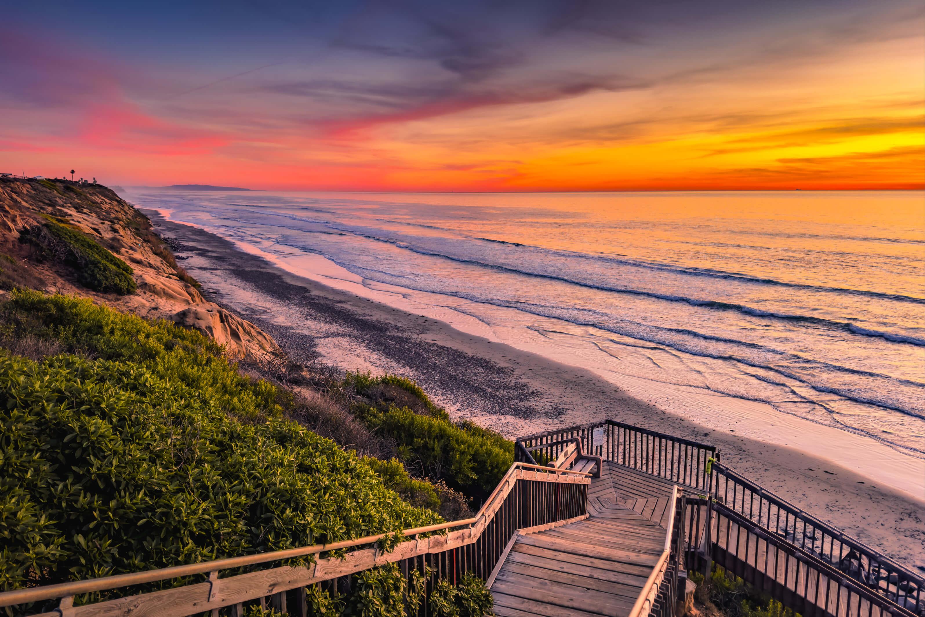 A staircase descends towards the beach, illuminated by the warm hues of a sunset sky in San Diego, California