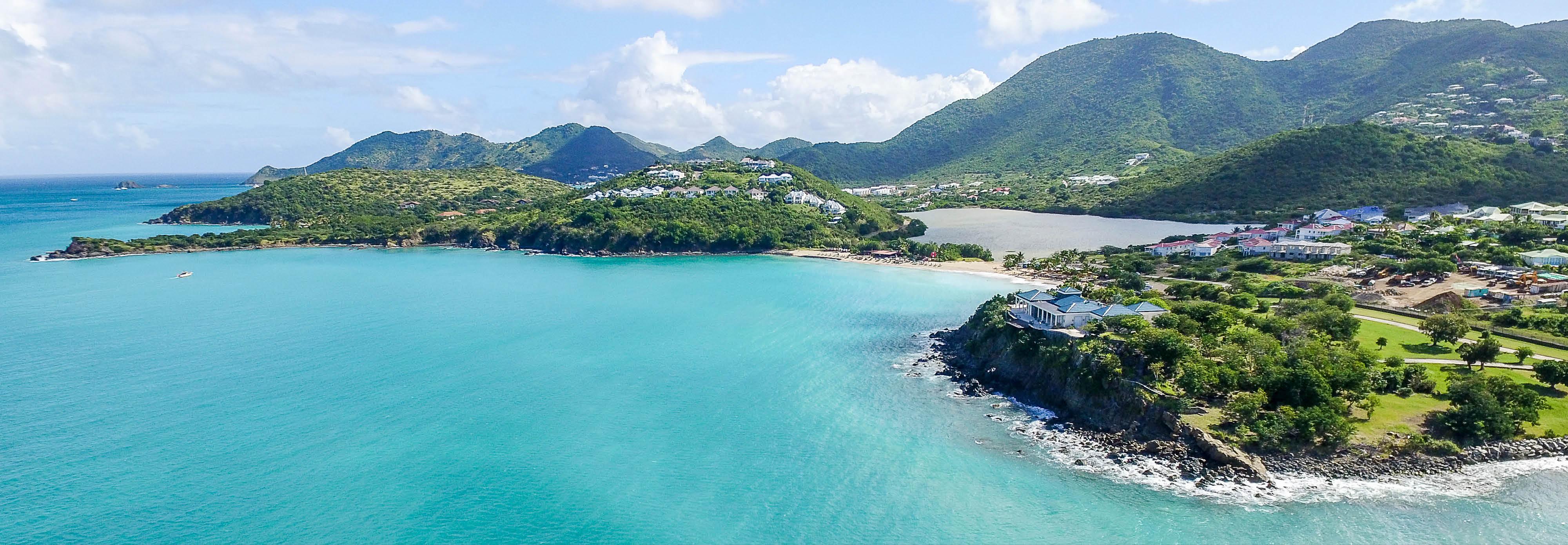 Azure ocean water up against lush shoreline and rising peaks of St. Martin