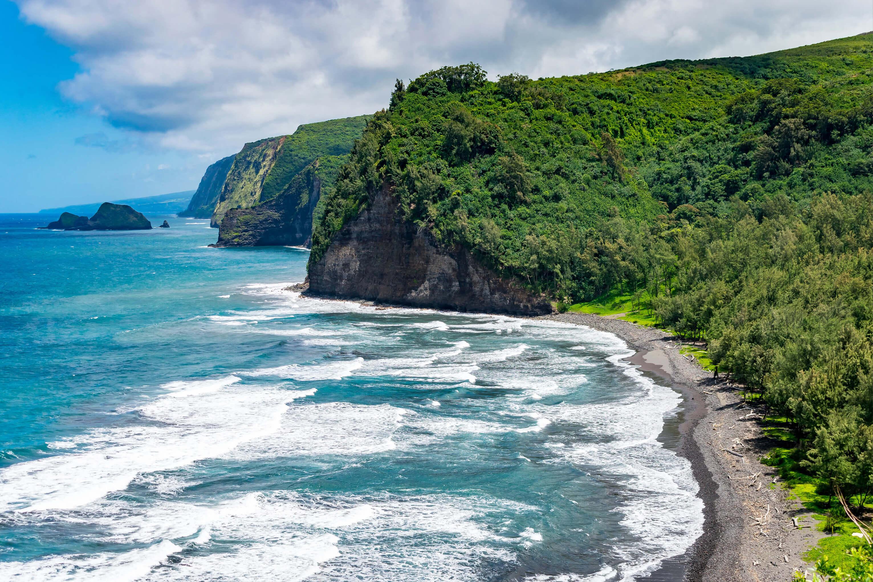 Waves crashing against a small beach on The Big Island in Hawaii, with lush greenery beyond the shore