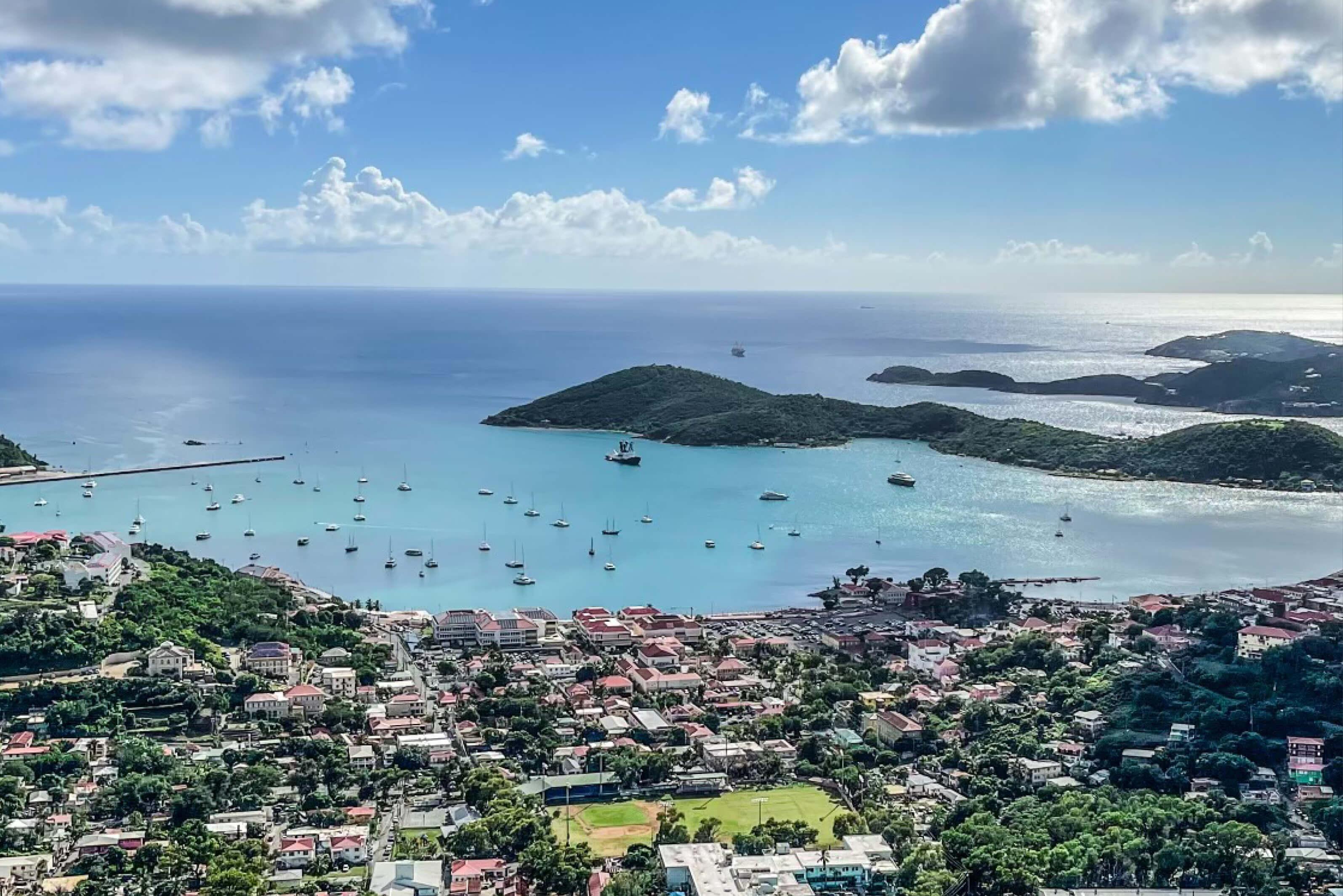 Boats anchored near the shore in U.S. Virgin Islands, with rolling hills going out to sea and a small coastal village