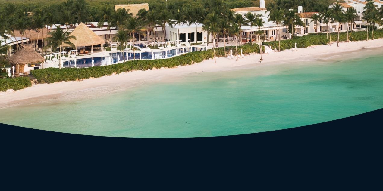 Aerial view of a large, luxurious Royalton resort complex featuring beachfront pools, thatched-roof cabanas, and white buildings lining a wide, pristine beach and turquoise ocean. Promotes a dual Royalton campaign.