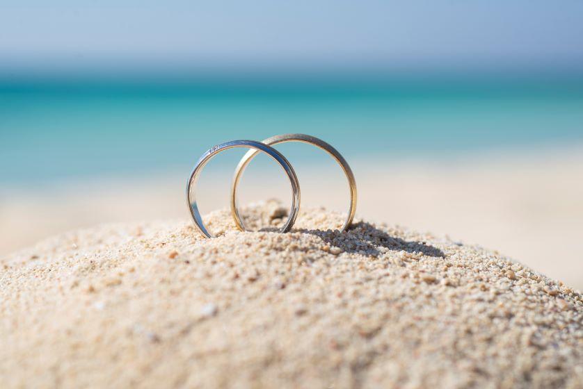 Two wedding rings in the sand with the ocean in the background.