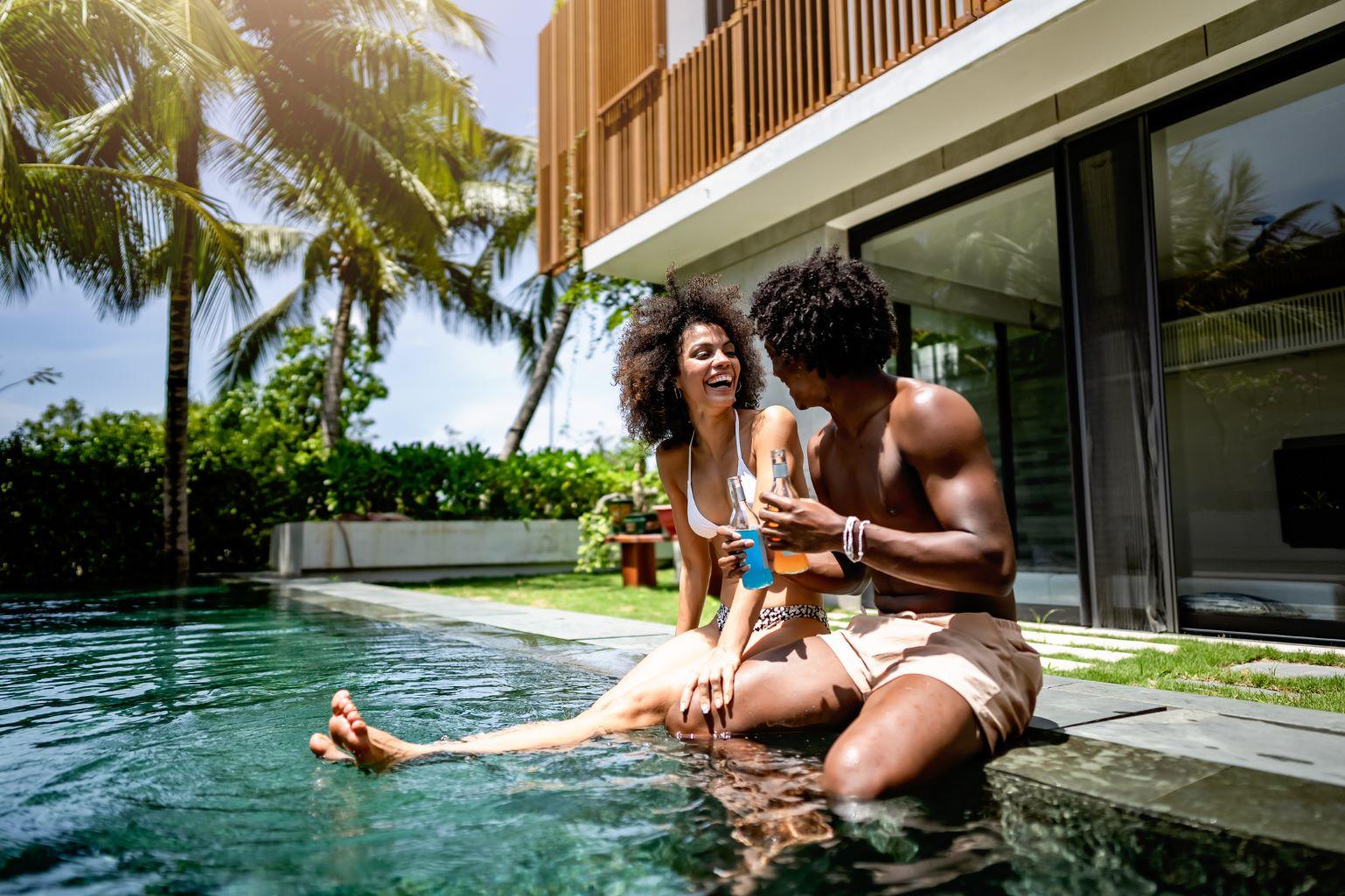 A happy couple relaxing by a swimming pool with drinks.