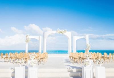 Beachfront wedding ceremony setup with white arches and seating featuring Majestic Resorts.
