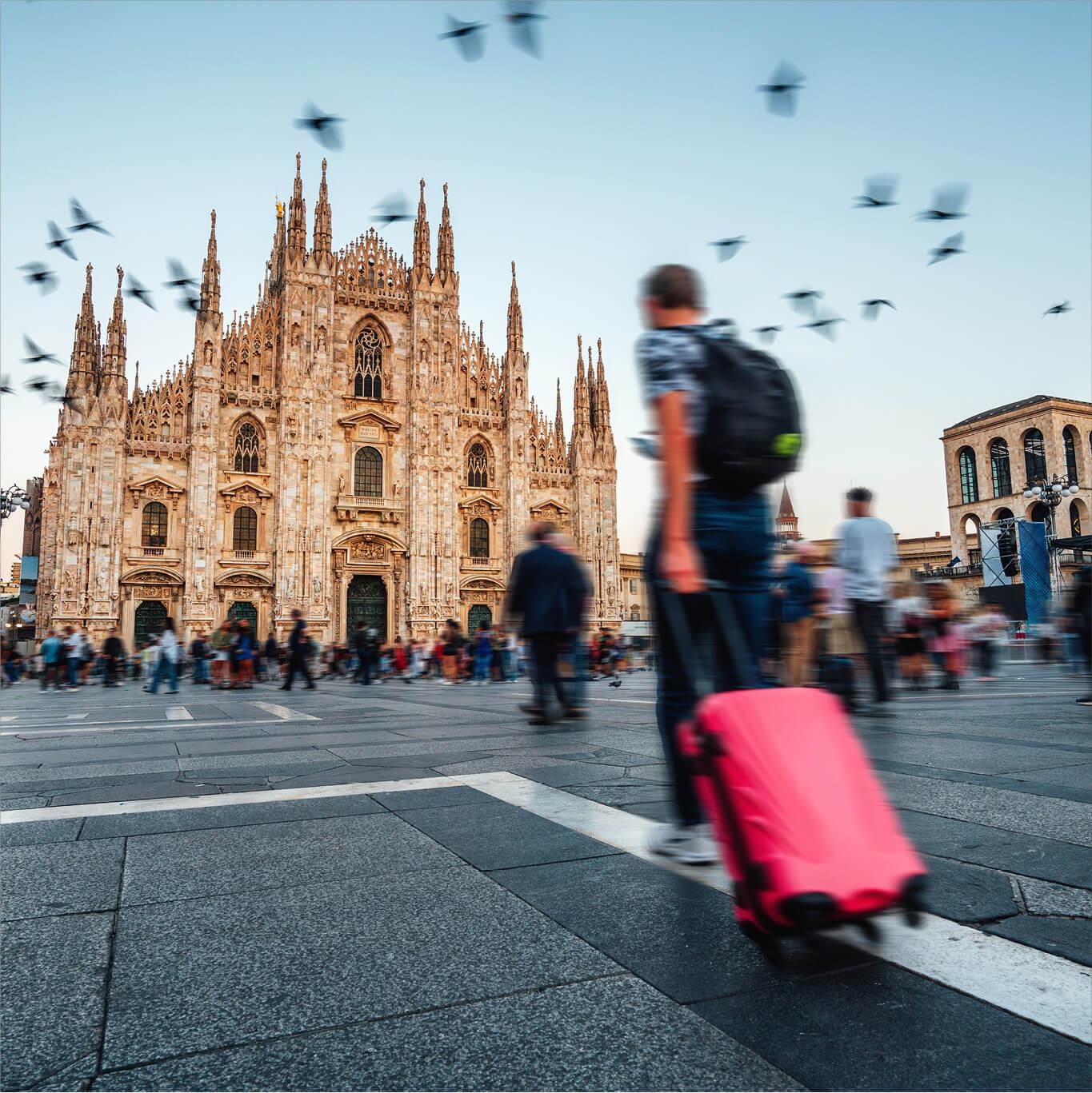 A traveler with a suitcase walks towards the Duomo di Milano