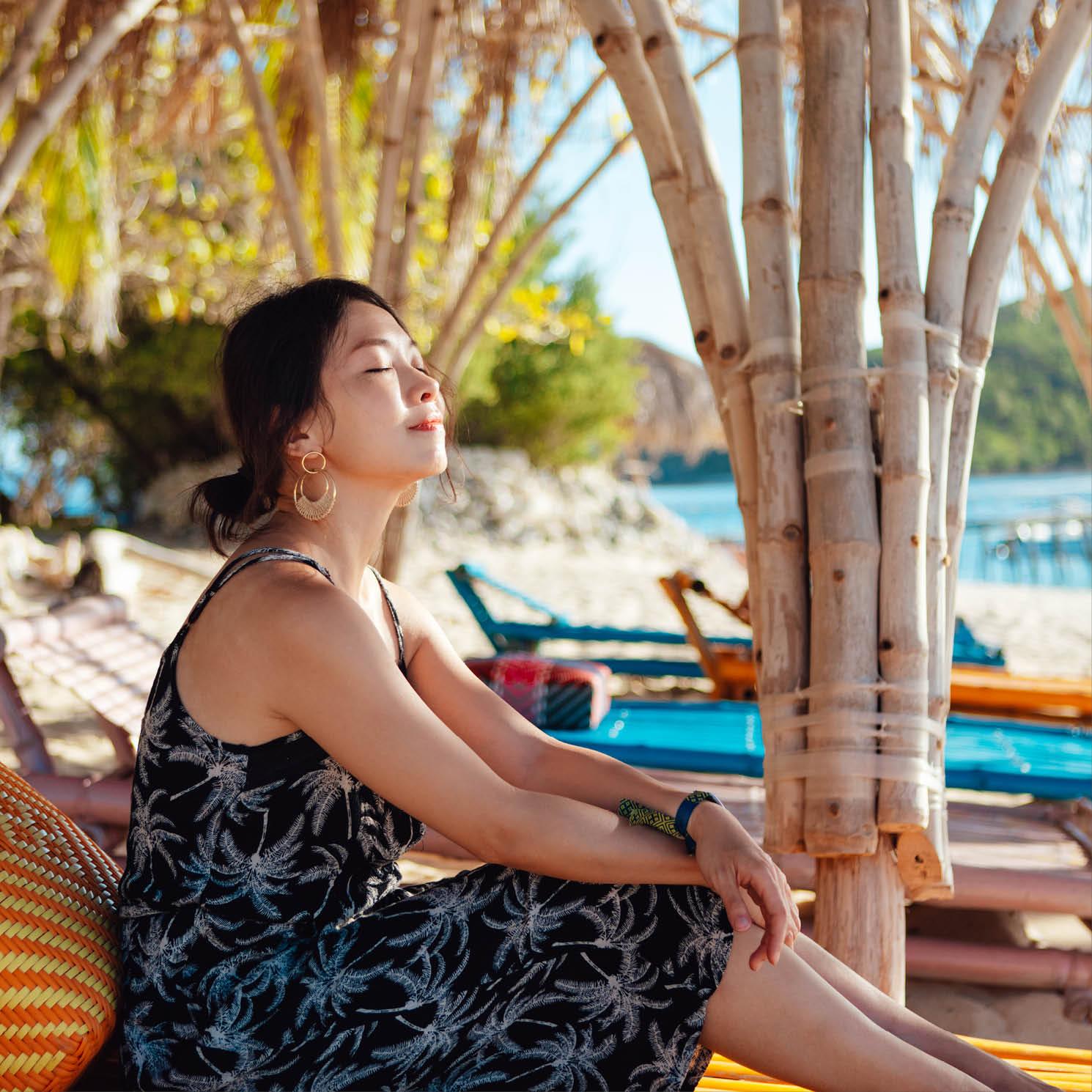 A woman relaxes with her eyes closed, on a lounge chair in a tropical setting