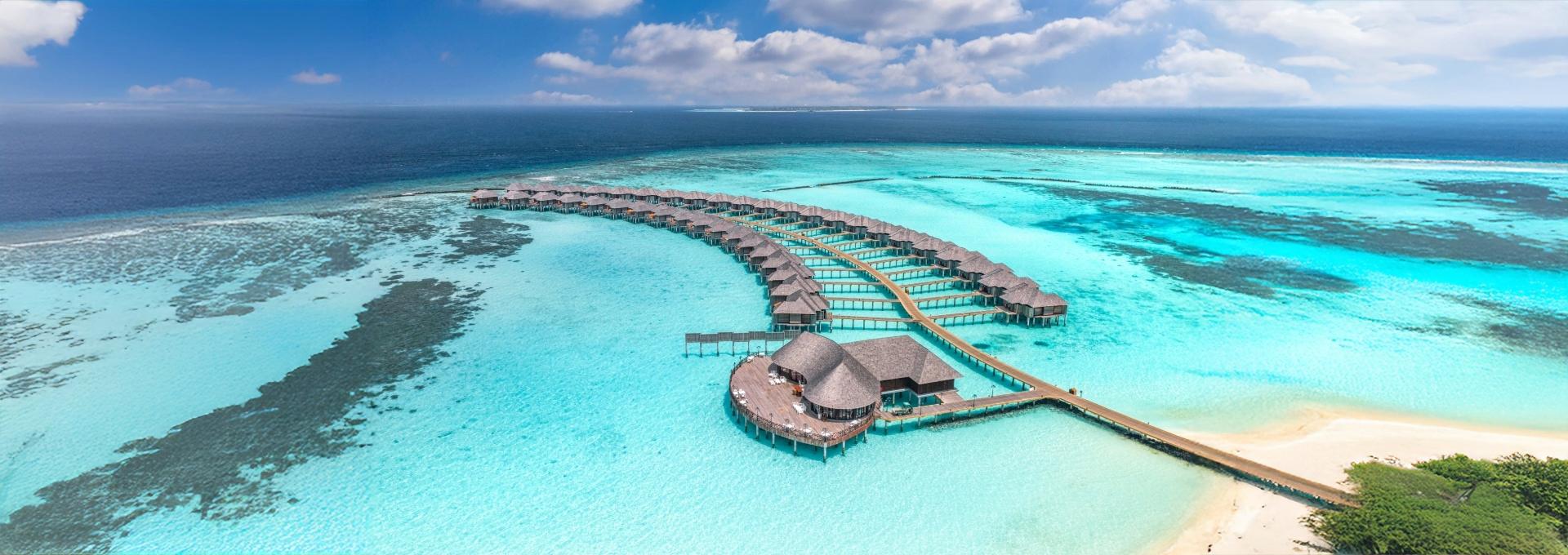 Aerial view of overwater bungalows extending into turquoise ocean water.