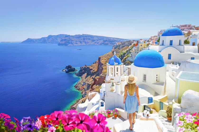 Traveler walking through Santorini with views of the caldera and blue-domed churches