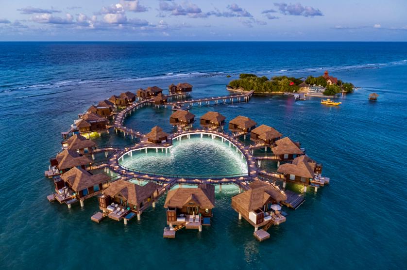 Aerial view of overwater bungalows surrounding a heart-shaped lagoon at a Sandals Caribbean Cay in Jamaica.